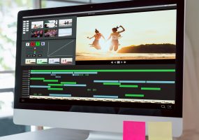 Concept of simple operation of blogger and vlogger, hand using computer on video editor works with footage on wooden table, camera and accessories on table.